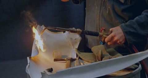 Metalworker uses blowtorch to shape metal panel in workshop