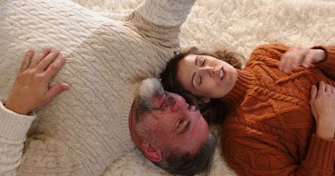 Cozy mature couple lying on plush rug wearing cable knit sweaters showing ring