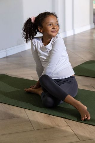 Girl practicing yoga at home on green mat, stretching and smiling in minimalist room