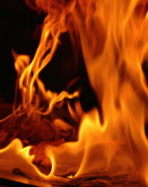 Visually striking close-up of intense flames against a dark background, highlighting the dynamic movement of the fire. Ideal for use in projects related to fire safety, energy, emergency services, or intense emotions and drama in visual arts.