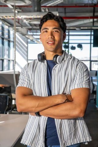 Young asian professional posing confidently with headphones and smartwatch in modern open-plan offic