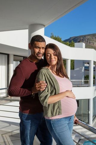 Romantic moment with diverse pregnant couple on modern balcony