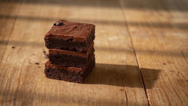 Sunlit fudgy chocolate brownie stack close-up on rustic wooden table with long shadow