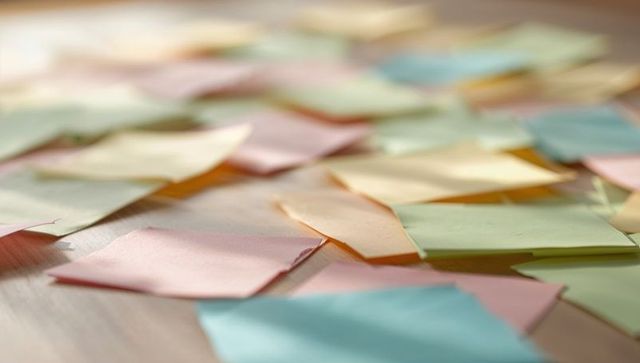 Scattering pastel sticky notes resting on wooden tabletop catching warm sunlight