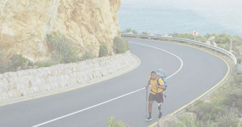 Solo hiker trekking along winding coastal road with backpack and poles overlooking sea and cliffs