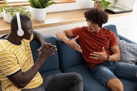 Diverse Friends Communicating Using Headphones on Sofa
