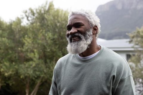 Smiling senior African American man wearing sage crewneck standing in backyard garden
