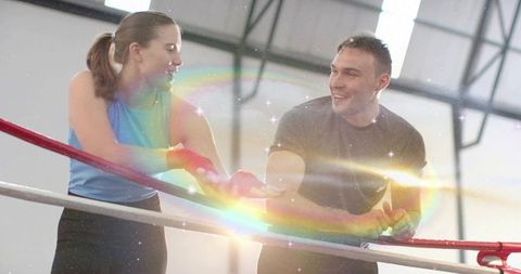 Boxing partners training and laughing on ring ropes with rainbow lens flare