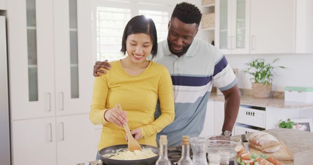 This joyful picture of a diverse couple cooking together in a modern kitchen embodies sharing quality time and building a strong bond at home. Ideal for advertising lifestyle brands, family-oriented products, home and kitchenware, recipe blogs, and articles about relationship tips. It reflects themes of cooperation, love, and the joys of preparing meals together.