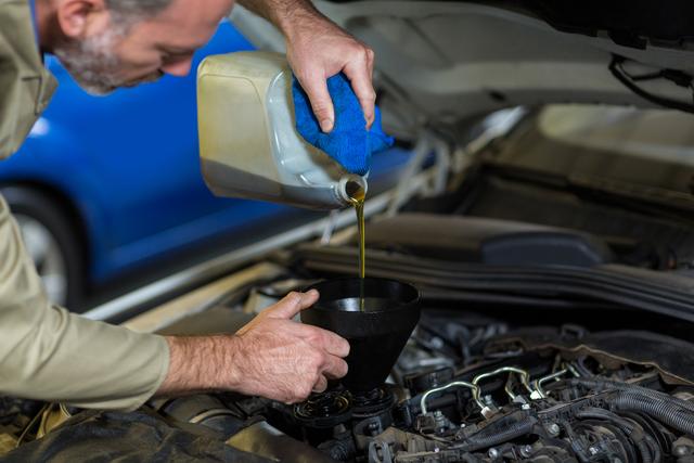 Mechanic pouring oil into car engine in repair garage. Ideal for illustrating automotive repair services, car maintenance guides, and professional mechanic services. Useful for websites, brochures, and advertisements related to auto repair shops and vehicle maintenance.