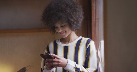 Biracial Woman Relaxing by Window Using Smartphone at Home