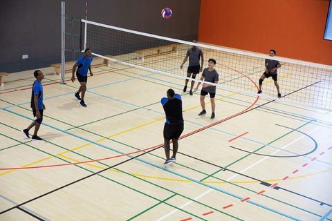 Men playing competitive indoor volleyball on marked gym court with diverse teams
