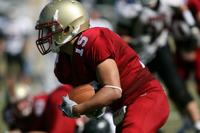 Football player running with the ball during a game, showcasing athletic action. Ideal for sports articles, athletic training features, or promotions related to team sports equipment and apparel.