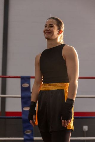 Female boxer standing in ring showing confidence and strength with hand wraps in spotlight