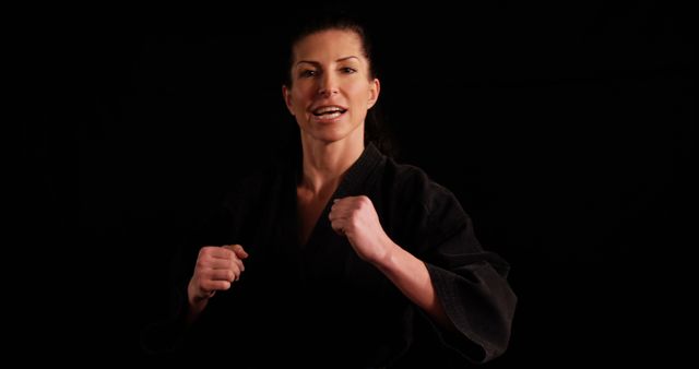 Female martial artist demonstrating aggressive fighting stance. She wears a black martial arts uniform and exudes determination and strength. This image is perfect for websites, blogs, or marketing materials related to martial arts training, women in sports, self-defense courses, fitness motivation, and empowerment.
