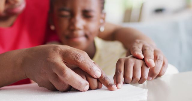 Parent guides child in reading braille, focusing on their hands and tactile education. Perfect for use in educational content, parenting resources, and awareness campaigns on disabilities and inclusion.