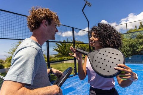 Sunlit padel coaching with diverse players holding paddles on vibrant blue court
