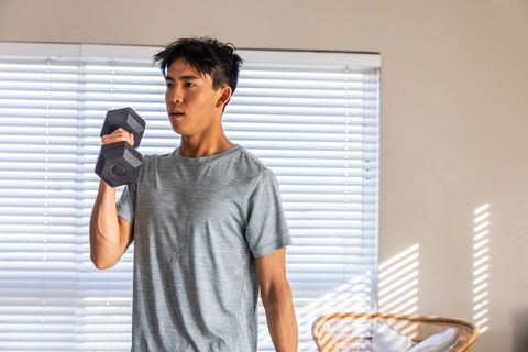 Asian man lifting dumbbell during home workout by sunlit window