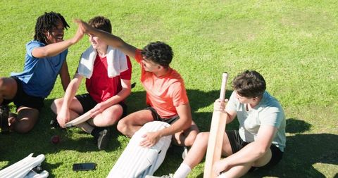 Youth cricket team celebrating practice break high-fiving on sunny grass field