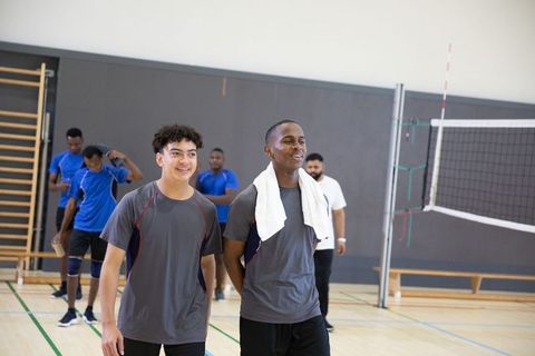 Smiling male volleyball teammates walking together in school gym carrying towel and talking