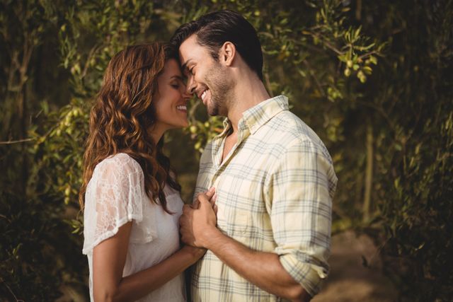 Young couple embracing and smiling at an olive farm, surrounded by trees. Perfect for use in advertisements, romantic greeting cards, relationship blogs, or lifestyle magazines focusing on love and nature.