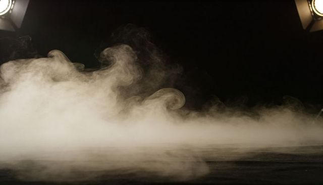 Rising dense fog curling across matte stage floor under dramatic studio spotlights