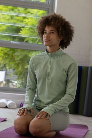 African american woman kneeling on yoga mat practicing mindful breathing in sunlit studio