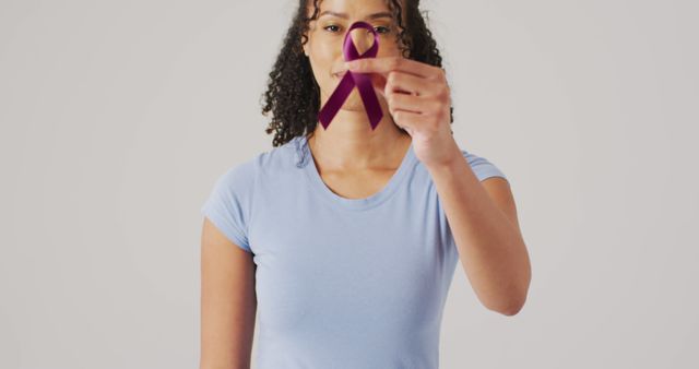 Woman standing holding purple awareness ribbon, symbolizing health awareness and support for various causes. Ideal for health campaigns, charity events, and nonprofit organizations promoting awareness and advocacy.