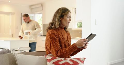 Couple relaxing in modern open-plan home woman using tablet man with coffee and phone