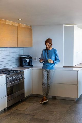 African american man leaning on sleek modern kitchen counter holding tablet and coffee mug