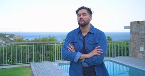 Confident man standing arms crossed on coastal pool deck overlooking ocean and horizon