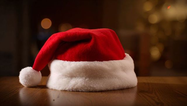 Red Santa Hat Resting on Wooden Table with Warm Holiday Bokeh Lights
