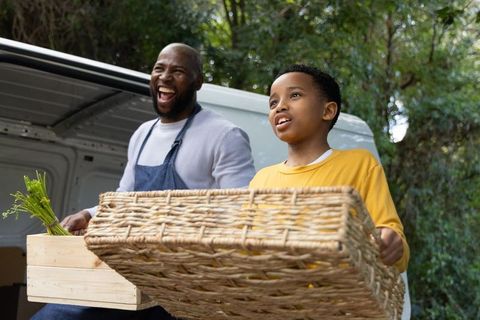 African american vendor and son carrying wicker basket of fresh produce by market van