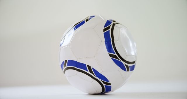A classic white soccer ball with black and blue patterns is positioned against a neutral background, with copy space. Its design suggests a traditional style, commonly used in sports and recreational activities.