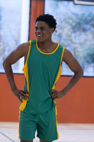 Smiling Basketball Player in Green and Yellow Jersey on Indoor Court