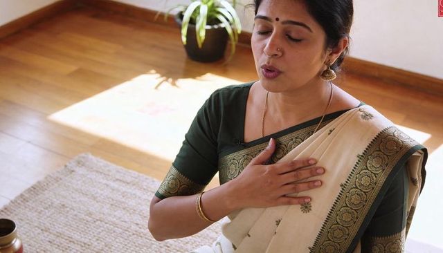 Serene woman wearing cream saree and green blouse singing with hand on chest while meditating