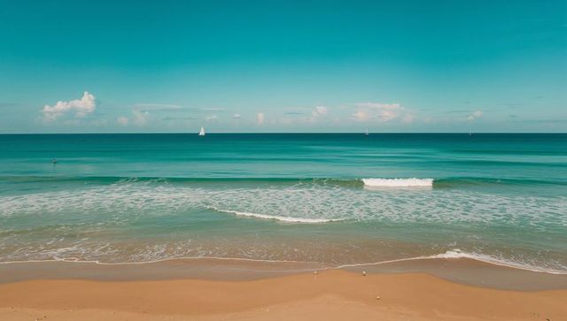Turquoise ocean horizon with white sailboats and gentle sandy shoreline