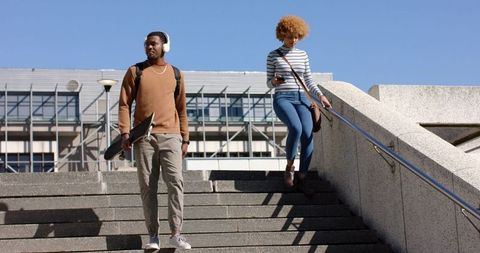 Diverse young adults walking down city stairs carrying skateboard and checking phone