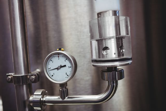 Close-up view of a pressure gauge attached to a stainless steel storage tank in a brewery. Ideal for illustrating industrial equipment, brewing processes, and the precision involved in beer production. Useful for articles, blogs, and presentations on brewing technology, manufacturing, and engineering.