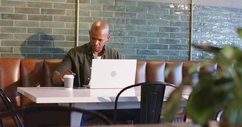 Man working on laptop in cafe booth with coffee cup and smartphone