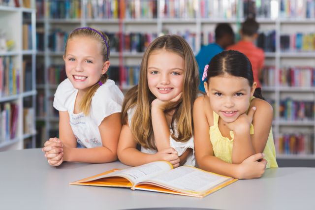 Three young girls are reading a book together in a library, showcasing a collaborative learning environment. This image is ideal for educational content, school websites, literacy programs, and children's book promotions.