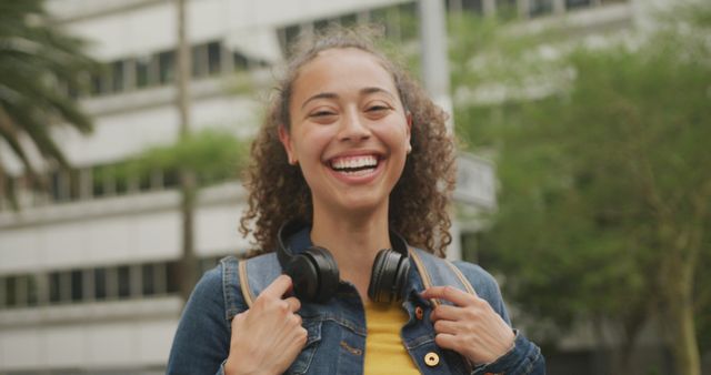 Portrait of happy biracial woman in city, wearing headphones and smiling. digital nomad on the go, out and about in the city.