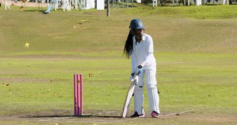 Young cricketer standing at crease wearing helmet and pads holding bat near pink stumps
