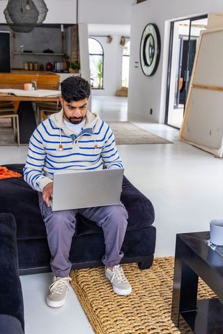 Indian man working on laptop in modern minimalist living room for remote work lifestyle