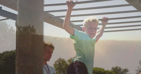 Boy Swinging on Monkey Bars with Supervisor at Playground