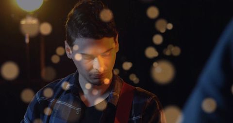 Young musician playing electric guitar under warm spotlight with bokeh and moody lighting