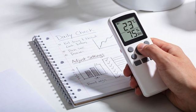 Handheld digital thermometer hygrometer showing 23°c 75% rh over notebook checklist