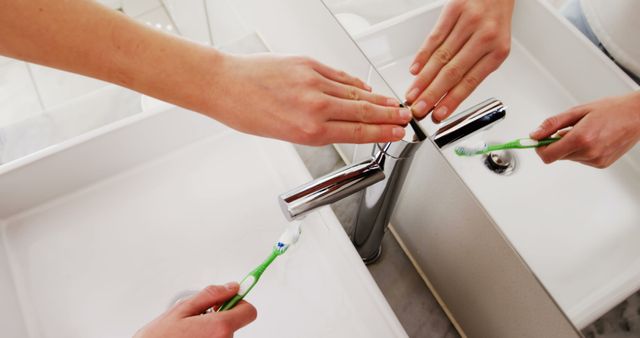 Person washing a toothbrush under faucet in a bathroom emphasizes personal hygiene and oral care. Useful for publications and advertisements related to dental health, hygiene products, and daily routines.