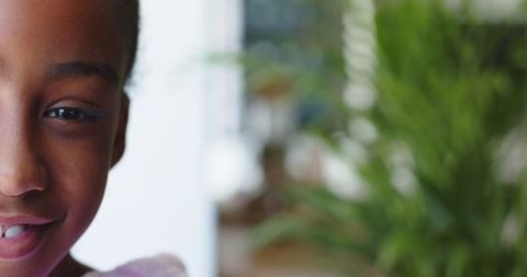 Closeup african american girl smiling by window with green plant and soft daylight
