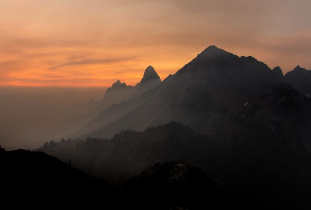 Mountain peaks silhouetted against a twilight sky with a serene mist enveloping the landscape. Perfect for nature and travel websites, offering a tranquil and scenic view of the wilderness.
